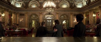 Movie still from “John Wick: Chapter 2” (2017), directed by Chad Stahelski – Two men in suits are holding hands in front of a chandelier in an ornate room; Wide shot, Low angle
