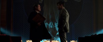 Movie still from “John Wick: Chapter 2” (2017), directed by Chad Stahelski – Two men standing next to each other in front of candles; Medium shot, Over the shoulder angle