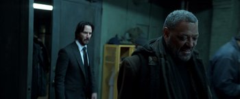 Movie still from “John Wick: Chapter 2” (2017), directed by Chad Stahelski – A man in a suit and tie standing next to another man in a coat; Medium shot, Over the shoulder angle