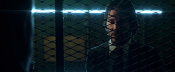 Movie still from “John Wick: Chapter 2” (2017), directed by Chad Stahelski – A man in a suit looking through a fence at night; Close Up shot, Low angle