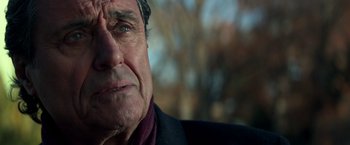 Movie still from “John Wick: Chapter 2” (2017), directed by Chad Stahelski – An older man with a black jacket and a purple scarf; Close Up shot, Over the shoulder angle