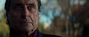 Movie still from “John Wick: Chapter 2” (2017), directed by Chad Stahelski – An older man with a black jacket and a purple shirt; Close Up shot, Over the shoulder angle