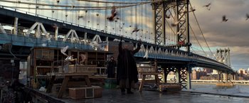 Movie still from “John Wick: Chapter 2” (2017), directed by Chad Stahelski – A man standing in front of a bridge with birds flying in the air; Wide shot, Low angle