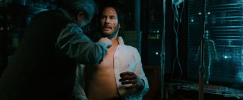 Movie still from “John Wick: Chapter 3 - Parabellum” (2019), directed by Chad Stahelski – A man is getting his chest waxed by another man; Medium shot, Over the shoulder angle