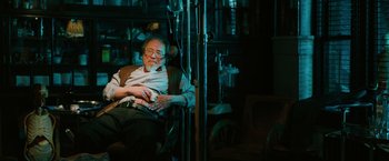 Movie still from “John Wick: Chapter 3 - Parabellum” (2019), directed by Chad Stahelski – An older man sitting in a chair in a dark room; Medium shot, High angle