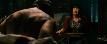 Movie still from “John Wick: Chapter 3 - Parabellum” (2019), directed by Chad Stahelski – A woman sitting at a table with a man sitting at her side; Medium shot, Over the shoulder angle