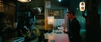 Movie still from “John Wick: Chapter 3 - Parabellum” (2019), directed by Chad Stahelski – Two men sitting at a counter in front of a lamp; Medium shot, Low angle