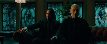 Movie still from “John Wick: Chapter 3 - Parabellum” (2019), directed by Chad Stahelski – Two men sitting on a couch in front of a window; Medium shot, Low angle