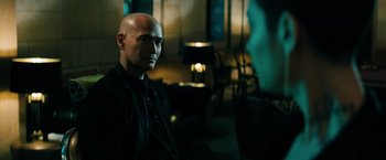 Movie still from “John Wick: Chapter 3 - Parabellum” (2019), directed by Chad Stahelski – A man with bald head sitting in a dark room; Close Up shot, Over the shoulder angle