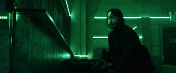 Movie still from “John Wick: Chapter 3 - Parabellum” (2019), directed by Chad Stahelski – A man holding a gun in front of green lights; Medium shot, Low angle