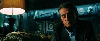 Movie still from “John Wick: Chapter 3 - Parabellum” (2019), directed by Chad Stahelski – An older man sitting on a couch in front of a fireplace; Close Up shot, Low angle