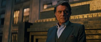 Movie still from “John Wick: Chapter 3 - Parabellum” (2019), directed by Chad Stahelski – A man in a suit and tie standing in front of stairs; Close Up shot, Over the shoulder angle