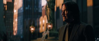 Movie still from “John Wick: Chapter 3 - Parabellum” (2019), directed by Chad Stahelski – A man wearing a suit and tie standing in front of a statue; Medium shot, Over the shoulder angle