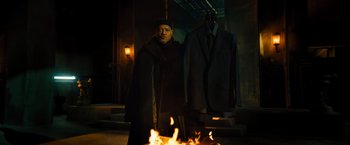 Movie still from “John Wick: Chapter 4” (2023), directed by Chad Stahelski – A man standing in front of a fire with a suit on it; Medium shot, Over the shoulder angle