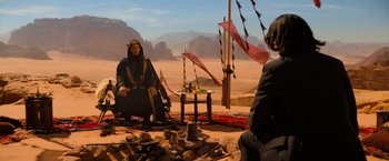 Movie still from “John Wick: Chapter 4” (2023), directed by Chad Stahelski – A man sitting on the ground in front of another man in the desert; Wide shot, Over the shoulder angle