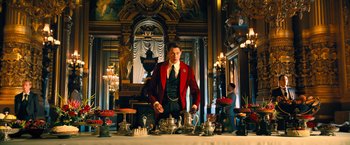 Movie still from “John Wick: Chapter 4” (2023), directed by Chad Stahelski – A man in a red jacket standing in front of a table with tea pots; Wide shot, Low angle