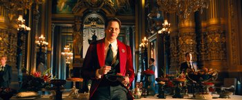 Movie still from “John Wick: Chapter 4” (2023), directed by Chad Stahelski – A man in a red jacket holding a glass; Medium shot, Low angle