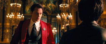 Movie still from “John Wick: Chapter 4” (2023), directed by Chad Stahelski – A man in a red jacket standing next to a chandelier; Medium shot, Over the shoulder angle