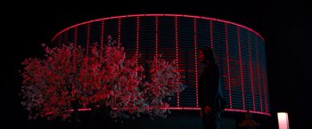 Movie still from “John Wick: Chapter 4” (2023), directed by Chad Stahelski – A woman standing next to a tree in front of a building; Extreme Wide shot, Low angle
