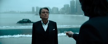 Movie still from “John Wick: Chapter 4” (2023), directed by Chad Stahelski – An older man wearing a suit standing next to a body of water; Medium shot, Over the shoulder angle