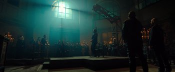 Movie still from “John Wick: Chapter 4” (2023), directed by Chad Stahelski – A group of people standing on a stage in front of a crowd; Wide shot, Low angle