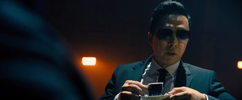 Movie still from “John Wick: Chapter 4” (2023), directed by Chad Stahelski – A man in a suit and sunglasses eating a sandwich; Close Up shot, Low angle