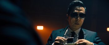 Movie still from “John Wick: Chapter 4” (2023), directed by Chad Stahelski – A man in a suit and sunglasses holding a camera; Close Up shot, Low angle