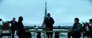 Movie still from “John Wick: Chapter 4” (2023), directed by Chad Stahelski – A man in a black suit and hat standing in front of an eiffel tower; Wide shot, Low angle