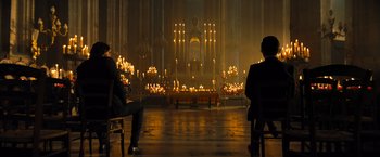 Movie still from “John Wick: Chapter 4” (2023), directed by Chad Stahelski – Two people sitting in chairs in front of candles in a church; Wide shot, High angle