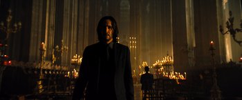 Movie still from “John Wick: Chapter 4” (2023), directed by Chad Stahelski – A man in a suit and tie standing in front of candles in a room; Medium shot, Low angle