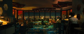 Movie still from “John Wick: Chapter 4” (2023), directed by Chad Stahelski – A person sitting at a desk in a room with a view of a city; Extreme Wide shot, High angle