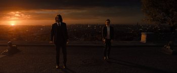 Movie still from “John Wick: Chapter 4” (2023), directed by Chad Stahelski – Two men standing on a hill at night with a city in the background; Wide shot, Low angle