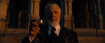 Movie still from “John Wick: Chapter 4” (2023), directed by Chad Stahelski – An older man holding a glass of wine in his hand; Medium shot, Low angle