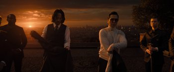 Movie still from “John Wick: Chapter 4” (2023), directed by Chad Stahelski – Two men sitting on top of a hill with a city in the background; Medium shot, Low angle