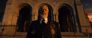 Movie still from “John Wick: Chapter 4” (2023), directed by Chad Stahelski – An older man in a suit and tie standing in front of a building; Medium shot, Low angle