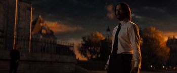 Movie still from “John Wick: Chapter 4” (2023), directed by Chad Stahelski – A man standing in front of a fence at dusk; Medium shot, Low angle