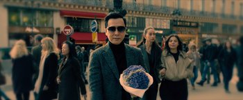 Movie still from “John Wick: Chapter 4” (2023), directed by Chad Stahelski – A man holding a bouquet of flowers in a street; Medium shot, Low angle