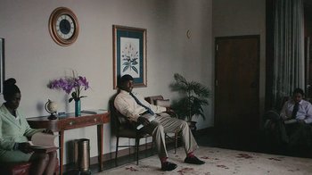 Movie still from “Atlanta” (2016), created by Donald Glover – A man sitting in a chair in front of a painting; Wide shot, Low angle