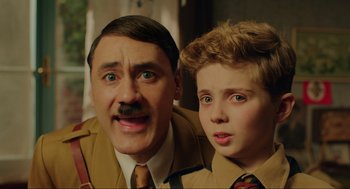 Movie still from “Jojo Rabbit” (2019), directed by Taika Waititi – A man and a boy are standing next to each other; Close Up shot, High angle