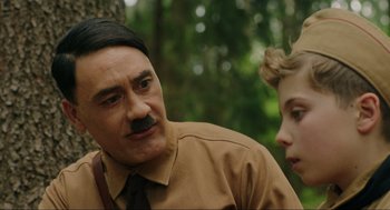 Movie still from “Jojo Rabbit” (2019), directed by Taika Waititi – A man and a woman in the woods with a mustache; Close Up shot, Over the shoulder angle