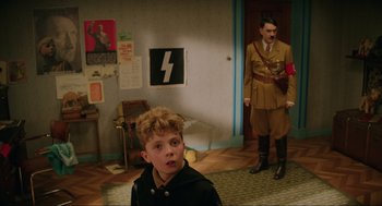 Movie still from “Jojo Rabbit” (2019), directed by Taika Waititi – A man in a uniform stands next to a boy in a room; Medium shot, Over the shoulder angle