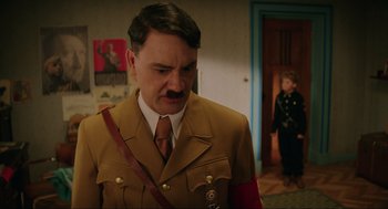 Movie still from “Jojo Rabbit” (2019), directed by Taika Waititi – A man in a military uniform standing next to a woman; Medium shot, Over the shoulder angle