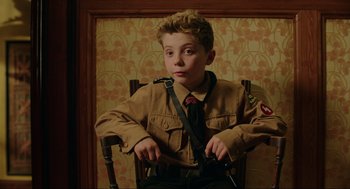 Movie still from “Jojo Rabbit” (2019), directed by Taika Waititi – A young boy in uniform sitting in a chair; Medium shot, High angle