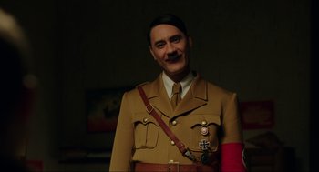 Movie still from “Jojo Rabbit” (2019), directed by Taika Waititi – A man dressed in a military uniform with a red arm bandage; Medium shot, Over the shoulder angle