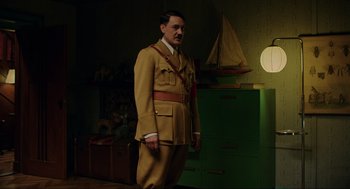 Movie still from “Jojo Rabbit” (2019), directed by Taika Waititi – A man in a suit and tie standing in a room; Medium shot, High angle