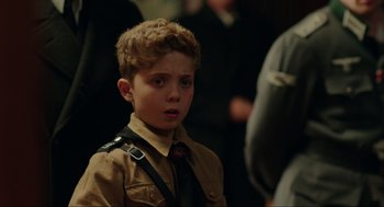 Movie still from “Jojo Rabbit” (2019), directed by Taika Waititi – A young boy wearing a brown shirt and a red neck tie; Close Up shot, Over the shoulder angle