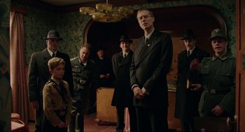 Movie still from “Jojo Rabbit” (2019), directed by Taika Waititi – A group of men in suits and hats standing in a room; Medium shot, Low angle