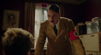 Movie still from “Jojo Rabbit” (2019), directed by Taika Waititi – A man in a suit and tie standing next to a window; Medium shot, Over the shoulder angle