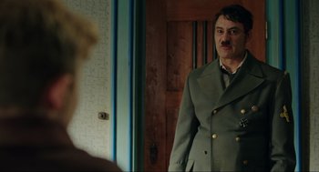 Movie still from “Jojo Rabbit” (2019), directed by Taika Waititi – A man wearing a suit and tie standing in front of a mirror; Medium shot, Over the shoulder angle