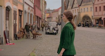 Movie still from “Jojo Rabbit” (2019), directed by Taika Waititi – A woman in a green jacket standing on a street; Medium shot, Over the shoulder angle
